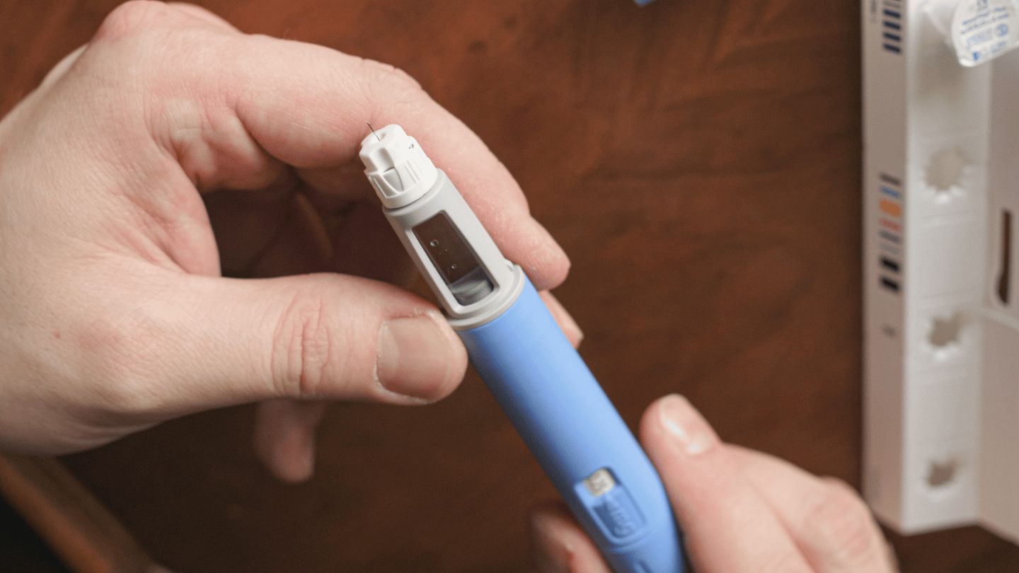 Close-up of a person holding a blue Ozempic injection pen, showcasing the small needle at the tip, used for administering the medication to manage blood sugar levels and aid in weight loss