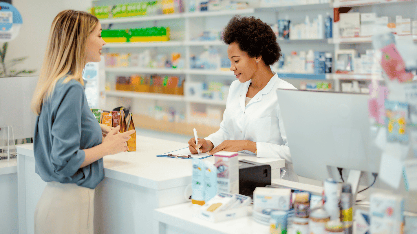 A woman consults with a pharmacist about Wegovy availability at a pharmacy counter. The pharmacist provides guidance on finding the weight loss medication