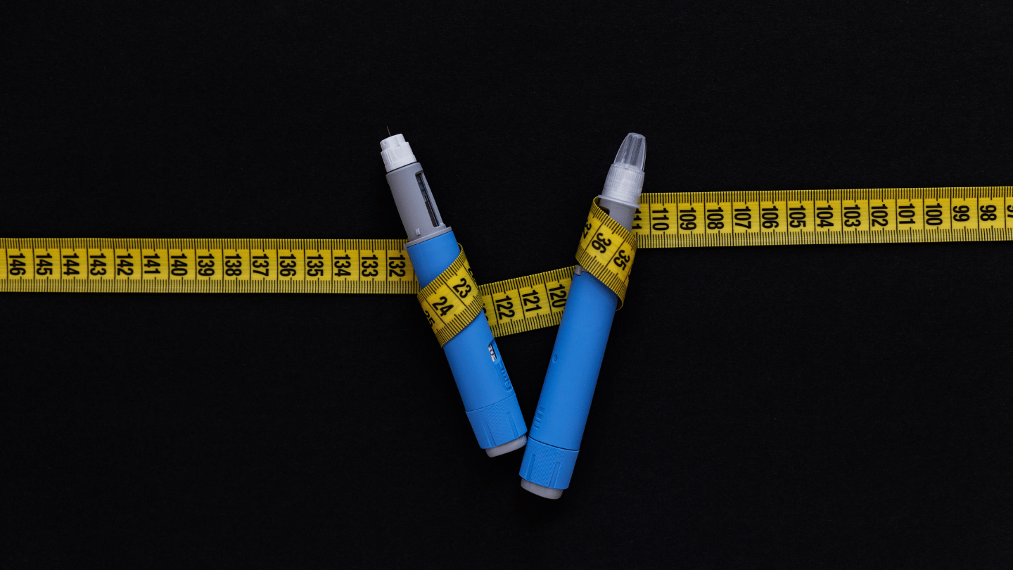 Two Ozempic injection pens wrapped in a yellow measuring tape, symbolizing its use for weight loss and diabetes management