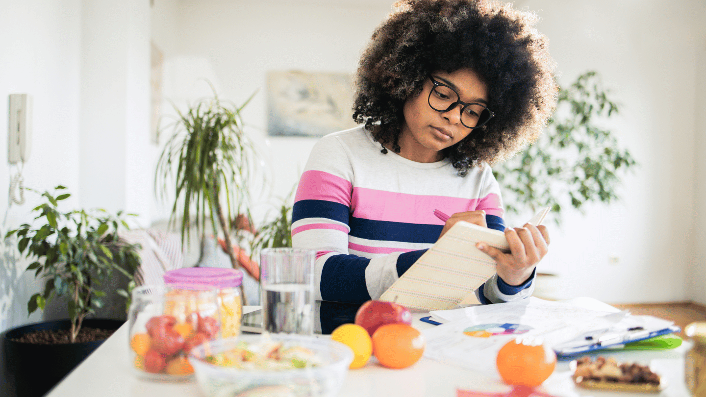 Person planning a semaglutide diet plan at home, writing in a notebook surrounded by healthy fruits and vegetables