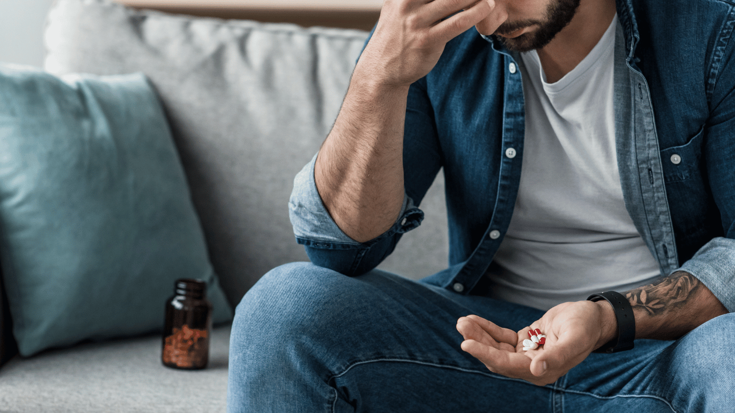 Man sitting on a couch holding pills, concerned about the risks and wondering, 'Can you overdose on Suboxone?' as he considers his treatment options