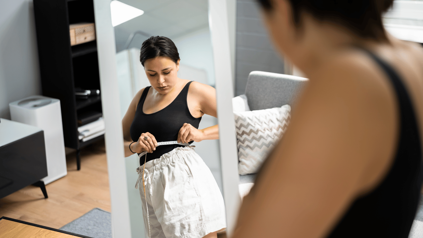 Woman measuring her waist in the mirror, trying to keep the weight off after Ozempic