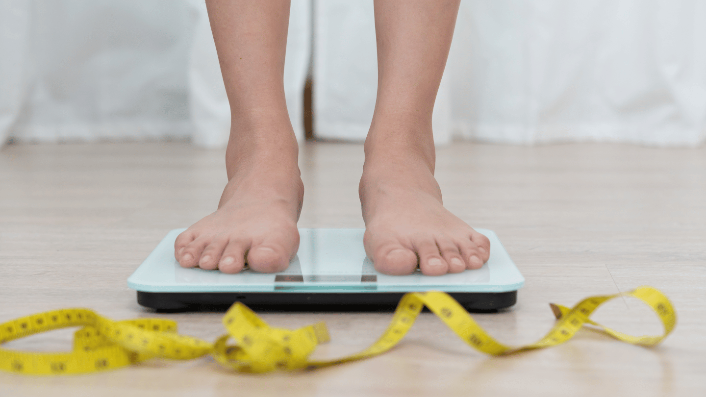 Person standing on a scale with a measuring tape on the floor, representing weight loss progress and Wegovy treatment options